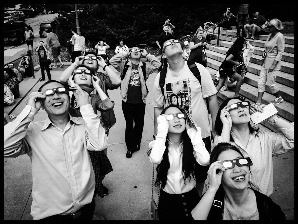 Fotografía en blanco y negro con una serie de personas con gafas de protección especiales para el sol mirando hacia arriba. Seguridad para poder ver el eclipse total de España 2026