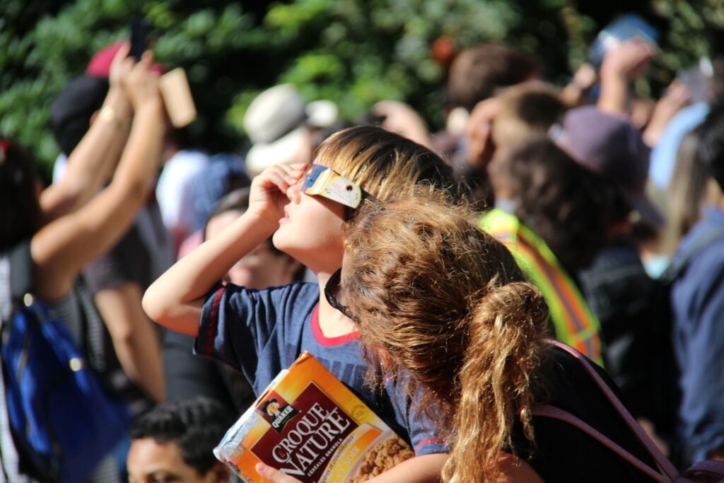 un niño mira al sol con unas gafas especiales mientras su madre le mira a él. Este será un evento para disfrutar en familia.